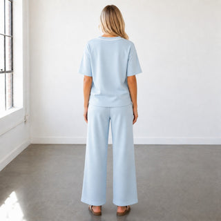 Blue scuba wide leg pants with relaxed fit and clean back silhouette styled with matching V-neck top, back view
