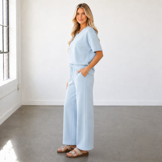 Blue scuba wide leg pants with wide leg silhouette, drawstring waist and pockets styled with matching V-neck top, side view