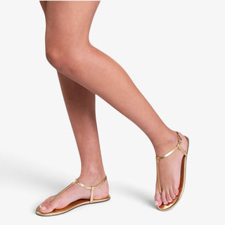 TKEES Mariana Gold flat sandals worn by a model, showing the metallic T-strap design and ankle buckle in a front lifestyle view for Game Day