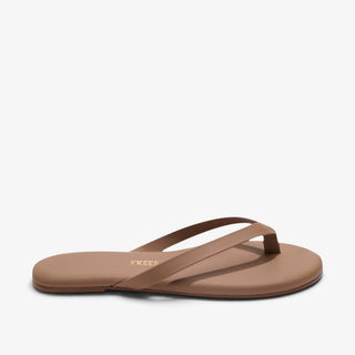 A single tan flat thong sandal shown from a side profile view against a clean white background. The brand name 'TKEES' is printed in gold on the insole.