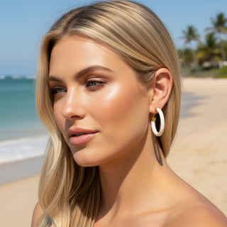 Model wearing Hoo Hoops white hoop earrings medium size with chunky acrylic design on tropical beach close-up view