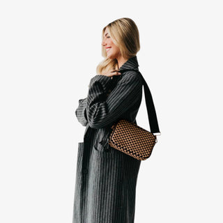 Woman wearing a Pretty Simple Woven Willow Camera Bag in checkered coffee and black with gold hardware, styled with a pinstripe blazer.
