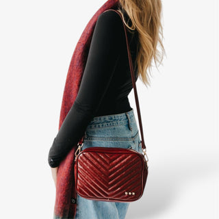 Burgundy quilted handbag worn by a person on a white background
