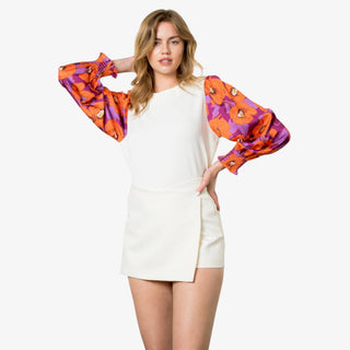 Woman wearing an ivory sweater with long puff sleeves in orange and purple floral print.
