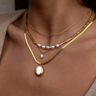 Gold herringbone pendant necklace layered with pearl necklaces close-up