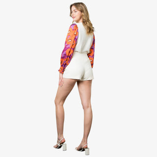 Woman wearing an ivory sweater with long puff sleeves in orange and purple floral print.