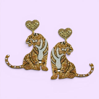 A pair of gold and white tiger beaded shaped earrings with heart-shaped studs, displayed on a light lavender background.