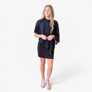 Black cape sleeve mini dress featuring a sheer draped overlay and fitted mini skirt, front view on model with hands gently clasped.