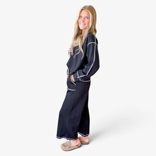 Women's black scuba knit two piece pant set featuring a relaxed long sleeve top, contrast stitching and wide leg pants, modeled from the side.