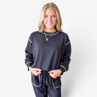 Black scuba knit women's lounge set showing contrast seam stitching on the crewneck top and sleeves, elastic drawstring waistband and front pockets, close-up view.