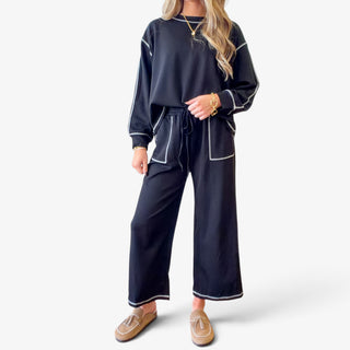 Women's black scuba knit matching set featuring a long sleeve crewneck top, drawstring waist pants, oversized patch pockets and contrast stitching, front view.