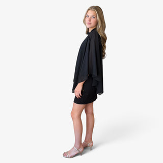 Black sheer cape overlay mini dress showing flowy asymmetrical cape sleeves, relaxed draping and fitted skirt, side view with silver heels.