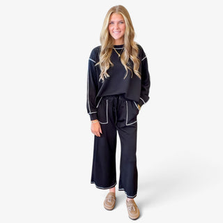  Women's black two piece scuba pant set with relaxed long sleeve sweatshirt, wide leg cropped pants, contrast stitching and front patch pockets, full outfit view.