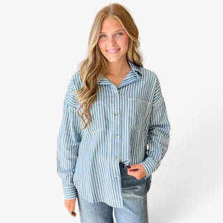  Blue striped button down shirt for women featuring white vertical stripes, collared neckline, two chest pockets, and relaxed fit, front view with jeans.