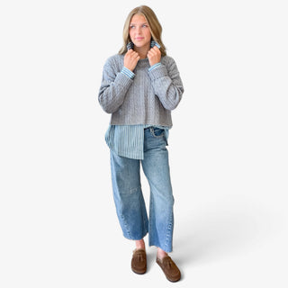 Women's blue striped button down shirt layered under a gray cable knit sweater, styled with barrel jeans and brown loafers, full-length outfit view.