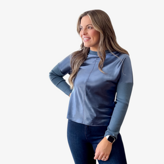 Woman wearing a blue long-sleeve metallic front top and dark jeans on a white background