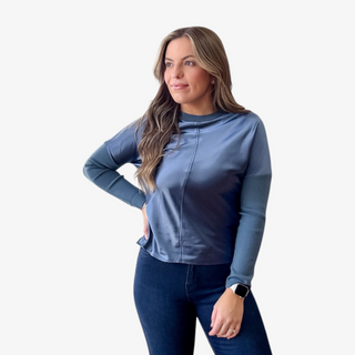 Woman wearing a blue long-sleeve metallic top and dark jeans on a white background