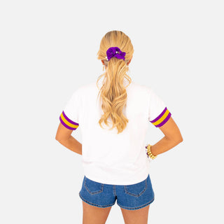 Back view of Brianna Cannon LSU Sparkle T-shirt in white with purple and gold striped short sleeves, styled with denim shorts.