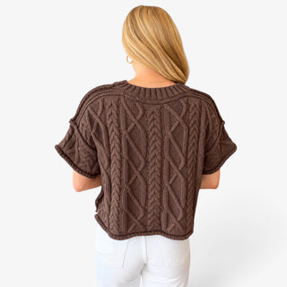 Brown cable knit sweater with textured braided knit pattern and relaxed short sleeves, back view on model with white pants.