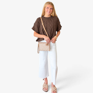Brown cable knit sweater styled with white pants, neutral sandals and crossbody bag, full outfit view on model.
