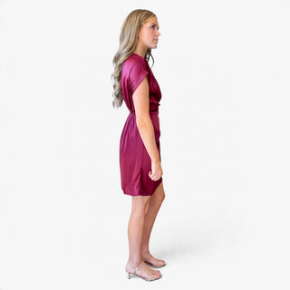 Burgundy satin fit and flare mini dress showing a defined waist, smooth satin finish and relaxed short sleeves, side profile with silver heels.