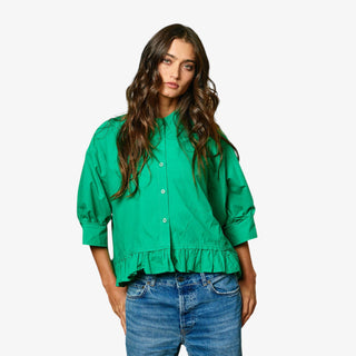 Woman wearing a green blouse with ruffled details and blue jeans on a white background
