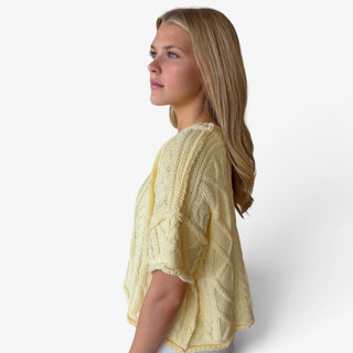 Butter yellow cable knit sweater with short sleeves, drop shoulders and relaxed silhouette styled with white jeans, side view