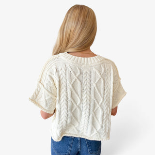 Off white cable knit sweater featuring textured cable stitching and relaxed cropped fit, back view on model.