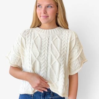 Off white cable knit sweater with short sleeves and textured knit detail styled with denim, front view.