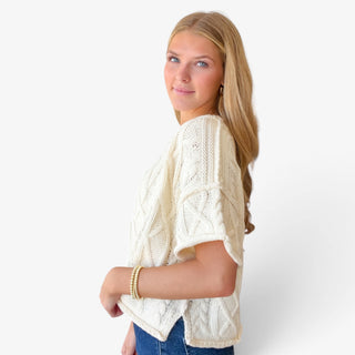Off white cable knit sweater with relaxed short sleeves and textured cable design, side view on model.