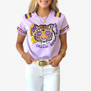 Close-up of lavender Callin Baton Rouge sequin tee with tiger graphic, game day sunglasses, and purple and gold sleeve stripes