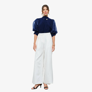 Woman wearing navy puff sleeve blouse with pleated detail and pearl accent