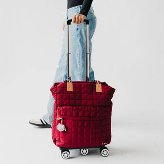 Red quilted suitcase with wheels held by a person on a light gray background