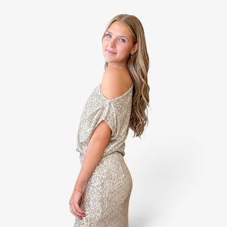 Champagne sequin one shoulder top with an exposed shoulder, relaxed draped fit and shimmering sequins, modeled from the side.