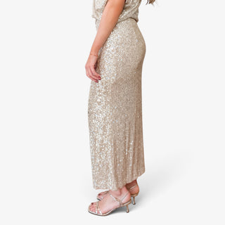 Champagne sequin side slit skirt with a flattering straight silhouette and ankle-length hem, modeled from the side with metallic heels.