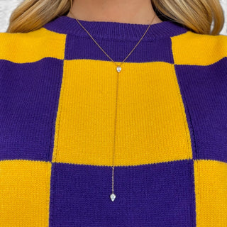 Close-up of purple and gold checkered game day sweater top showing the knit texture, bold checkerboard pattern and crew neckline