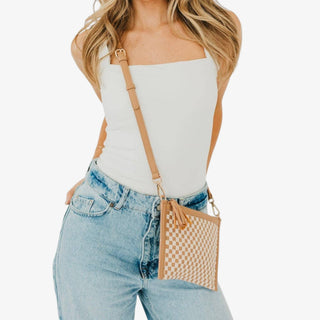 Tan woven crossbody clutch bag with cream checker pattern, wristlet strap, tassel and gold hardware shown carried at the hip in a front view.