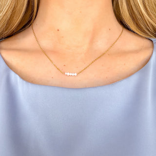 Dainty five pearl necklace featuring five white pearls centered on a delicate gold chain, styled on a model with a light blue top, front view.