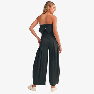 Black strapless barrel jumpsuit with wide cropped legs and foldover bodice styled with white sneakers front view