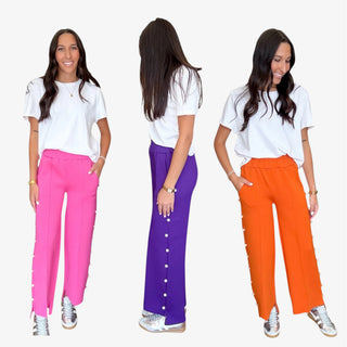 Woman modeling pink, purple, and orange pants with peal trim, paired with a white top on a white background