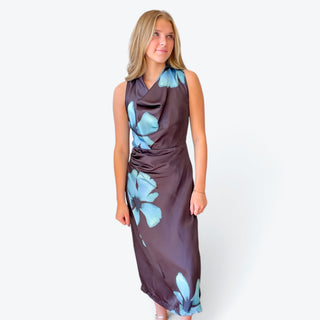 Brown satin-look floral midi dress featuring large blue flowers, a soft cowl neckline and flattering ruched waist, modeled from the front.