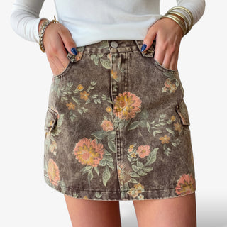 Floral denim cargo skirt featuring brown washed denim, vintage floral print, front pockets and cargo pocket details, close-up front view.