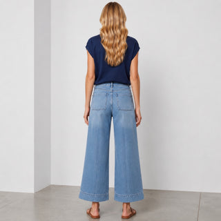 Back view of light wash front crease wide leg jeans with patch pockets and cropped wide leg silhouette styled with a navy cap sleeve top.