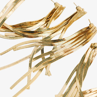 Gold tassel earrings featuring textured flat snake chain strands and gold post stud closures, extreme close-up detail view.