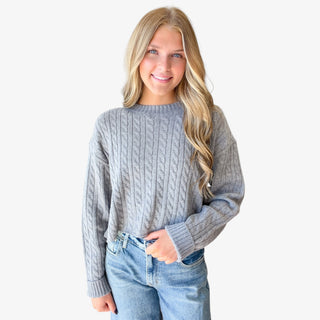 Gray cable knit sweater for women featuring a cropped silhouette, crew neckline, long sleeves, and ribbed cuffs, front view styled with jeans.