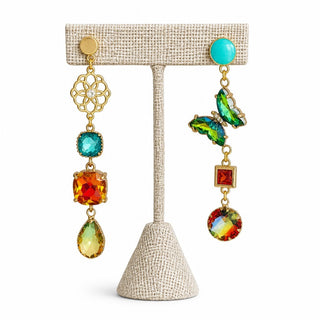 Green butterfly mismatched statement earrings with turquoise studs, gold floral detail and multicolor crystal drops displayed on an earring stand.