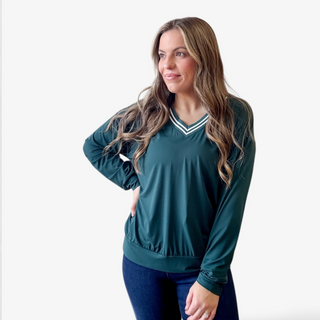 Forest green long sleeve V-neck top with striped trim paired with dark denim on a woman against a white background.