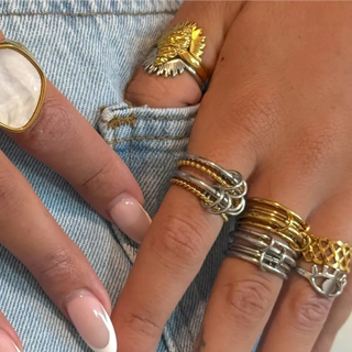 Close-up of hands wearing gold and silver ring stacks on a denim background