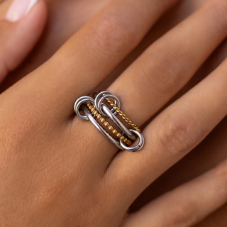 Close-up of a hand wearing a silver and gold ring stack on a neutral background