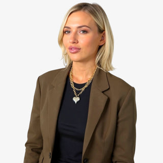 Model wearing a chunky gold chain necklace with a large silver heart pendant, styled with a blazer.
